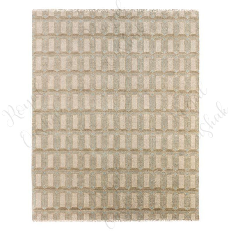 Puede incluir: Una alfombra rectangular con un patr&oacute;n geom&eacute;trico repetitivo de rect&aacute;ngulos verticales en color beige claro y gris suave. El dise&ntilde;o crea un efecto tridimensional con tonos claros y oscuros alternos, acabado con un fleco corto en los bordes.