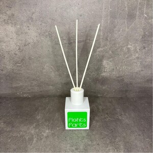 Könnte beinhalten: Ein weißer, quadratischer Raumduft-Diffusor mit drei dünnen, beigen Stäbchen, die oben eingesteckt sind. Auf der Vorderseite befindet sich ein leuchtend grünes, quadratisches Etikett mit dem Text Fights Farts in weißer, abgerundeter Schrift.