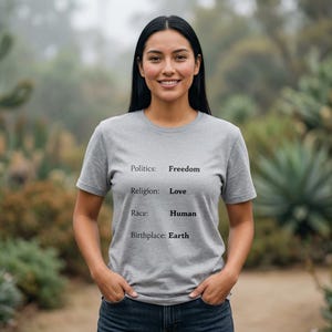 Op de afbeelding: Een grijs gemêleerd T-shirt met korte mouwen en zwarte tekst: Politics: Freedom, Religion: Love, Race: Human, Birthplace: Earth. Het shirt heeft een ronde hals en is gemaakt van een zachte, lichtgewicht stof met een standaard pasvorm.
