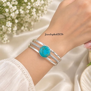 May include: A silver-toned cuff bracelet featuring three bands, with the outer bands having a hammered texture and the centre band displaying a ribbed pattern. A round, bright turquoise stone with brown matrix veins is set in the centre. Jewelryhub2026.