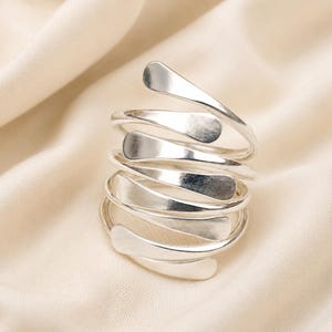 May include: A silver-toned ring featuring a multi-layered spiral design. The band consists of several overlapping coils that wrap around the finger, each ending in a flattened, rounded tip. The metal surface has a smooth, polished finish.
