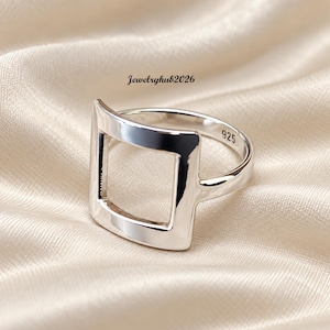 Puede incluir: Un anillo de plata pulida que presenta un diseño cuadrado abierto prominente en la parte frontal. La banda interior del anillo está claramente marcada con el número 925, indicando su composición. El texto Jewelryhub2026 es visible sobre el anillo.
