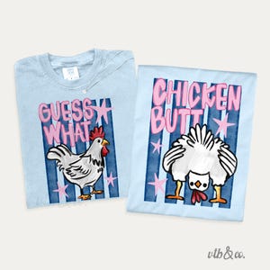 May include: Two light blue t-shirts with chicken-themed graphics. One shirt says "Guess What" with a chicken illustration. The other says "Chicken Butt" with a chicken's rear end. Both shirts have pink stars and blue stripes.