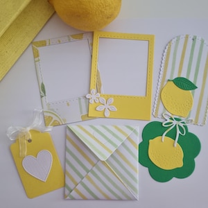 Peut inclure: Divers éléments de papeterie jaunes et blancs sur le thème du citron. Comprend deux cadres photo, une étiquette cadeau avec un cœur blanc, une enveloppe et deux découpes décoratives de citrons. Un citron entier est en arrière-plan.