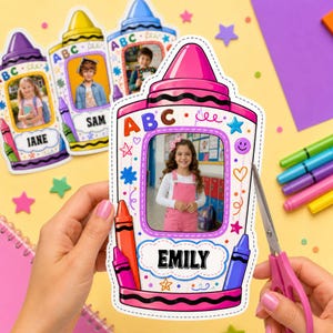 Pode incluir: Uma moldura de papel recortada em forma de giz de cera rosa com uma foto central de uma criança, o nome EMILY e ilustrações coloridas de ABC, estrelas e corações. O recorte tem uma borda pontilhada e é segurado durante o corte.