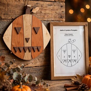 Pode incluir: Uma decoração de parede de madeira em forma de abóbora Jack-o'-Lantern feita de painéis verticais de madeira clara e escura com olhos, nariz e dentes triangulares, acompanhada por um modelo de papel emoldurado intitulado Jack-o'-Lantern Pumpkin.