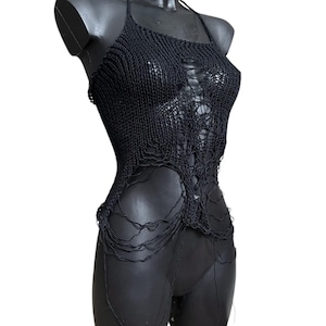 Puede incluir: Top negro con cuello halter y diseño desgastado de tejido abierto. El top presenta un escote cuadrado y una estética única y deshilachada. La prenda se exhibe en un maniquí negro, resaltando su textura y estilo. Una prenda distintiva.