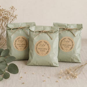 May include: Three sage green paper bags tied with twine bows. Each bag has a round sticker with the text "Everleaf Studio Potion making Tool Kit" inside a wreath design. A heart is below the text.