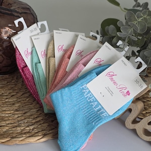 Può includere: Una collezione di calzini glitterati e colorati nei toni del rosa, verde acqua, oro e blu. Ogni paio ha un'etichetta con le parole "Snow Rose" e "PARFAITE". I calzini sono taglia 30-35.