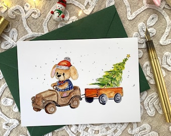 May include: A watercolour greeting card illustration featuring a tan puppy wearing a red Santa hat and blue plaid shirt, driving a brown wooden toy car that is pulling a small orange wagon containing a green Christmas tree with a yellow star.