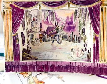 May include: A three-dimensional paper diorama depicting a stage scene with deep purple curtains and gold columns. The centre shows a ballet dancer and partner performing on a lake with white swans, set against a painted backdrop of trees and a building.