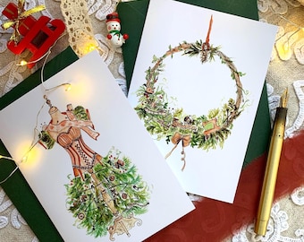 May include: Two white greeting cards featuring watercolour illustrations. One card displays a dress form adorned with pine branches and sewing notions. The second card shows a circular wreath made of greenery, pine cones, and sewing tools.