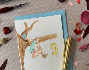 May include: A greeting card featuring a watercolour illustration of a person hanging from a tree branch, wearing a peach shirt and teal shorts, with a yellow number nine balloon floating nearby. The card is placed on a light blue envelope.