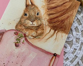 May include: A watercolour painting on paper featuring a brown rabbit with long ears resting its paws on the edge of a pink garment. The rabbit is positioned next to a small sprig of red clover flowers, with brown brushstrokes creating a textured effect.