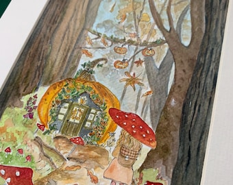 May include: A watercolour painting in a white mat frame depicting a forest scene with a pumpkin-shaped house, a person holding a red mushroom-patterned umbrella, scattered autumn leaves, and hanging jack-o'-lanterns among tall brown trees.