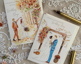 May include: Two white greeting cards with watercolour illustrations of wedding couples. One card shows a couple dancing in an autumn forest, the other shows a couple under a floral arch. Both cards feature the text Congratulations on your Wedding Day.