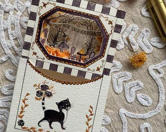 May include: A layered paper craft card featuring a black and white chequered border and a central cutout window. The interior scene depicts a forest with a banner reading HAPPY BIRTHDAY. The front panel shows a black cat with a floral tail design.