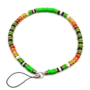 Könnte beinhalten: Ein farbenfroher Telefonanhänger mit scheibenförmigen Perlen in Grün, Schwarz, Weiß, Gold, Orange und Rot. Der Anhänger hat eine schwarze Schlaufe zum Befestigen am Telefon und einen silberfarbenen Verschluss.