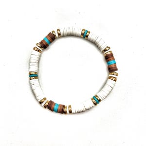 May include: White, brown, and turquoise beaded bracelet with gold accents. The bracelet features flat, disc-shaped beads in white, brown, and turquoise, separated by gold-colored spacers. A stylish accessory for everyday wear.