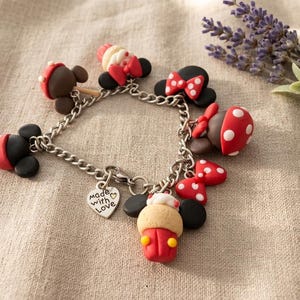 May include: A silver charm bracelet featuring multiple Mickey Mouse-themed charms. The charms include red and white polka-dotted bows, hats, and other decorative elements. A heart-shaped charm with the words "Made with Love" is also included.