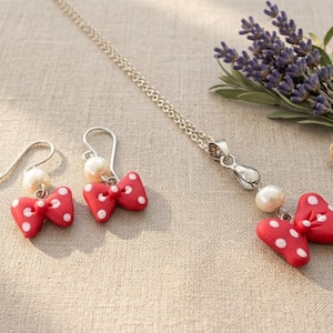 May include: A jewelry set featuring a silver necklace and earrings, each adorned with a red bow with white polka dots and a pearl. A small bouquet of lavender is tied with twine.