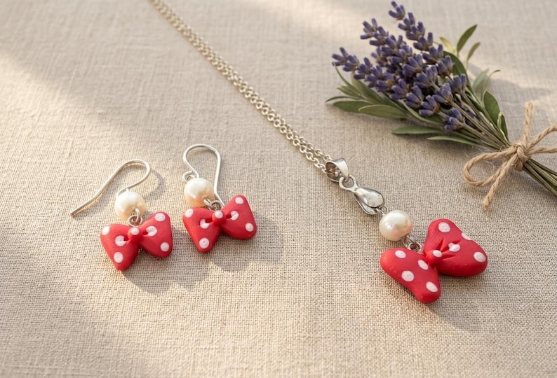 May include: A jewelry set featuring a silver necklace and earrings, each adorned with a red bow with white polka dots and a pearl. A small bouquet of lavender is tied with twine.