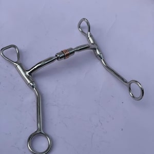 May include: A stainless steel horse bit with a copper centre link. The bit has a curved design with rings on each end and a loop on the top. The bit is designed for use in equestrian activities.