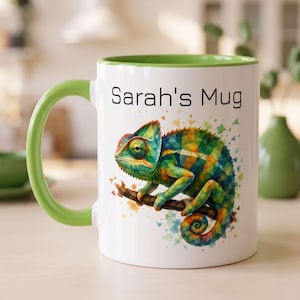Peut inclure: Un mug en céramique blanche avec une anse et un bord intérieur vert vif. L'extérieur présente une illustration géométrique colorée d'un caméléon perché sur une branche, entouré de petits triangles. Le texte Sarah's Mug est imprimé en noir.