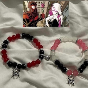 Pode incluir: Duas pulseiras de contas com tema Homem-Aranha. Uma pulseira apresenta contas vermelhas e pretas, a outra rosa, branca e preta. Cada pulseira tem um berloque de aranha prateada e um fecho de coração magnético.