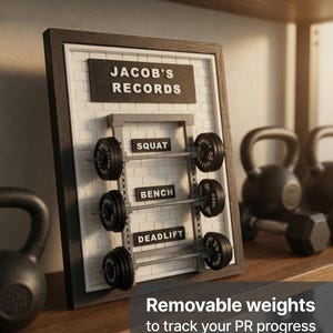 May include: A framed wall display featuring a white brick-patterned background with a black sign reading JACOB'S RECORDS. It includes three miniature barbell racks labelled SQUAT, BENCH, and DEADLIFT, each equipped with small, removable black weight plates.