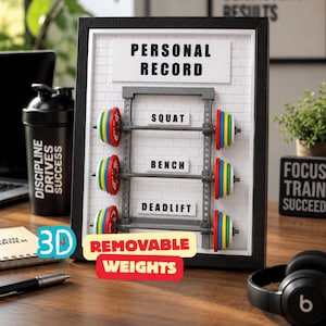 May include: A framed 3D weightlifting personal record board with removable weights. The board has the text "PERSONAL RECORD" at the top, with sections for "SQUAT", "BENCH", and "DEADLIFT". The weights are colorful and the text "3D REMOVABLE WEIGHTS" is also present.