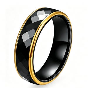 May include: A black ring with a faceted, geometric design. The ring has a gold-colored band on the top and bottom edges. The ring is set against a white background.