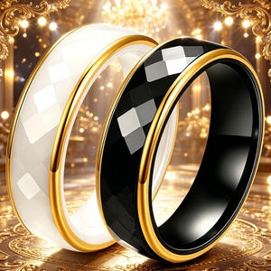 May include: Two rings, one white and one black, with a faceted design. Both rings have a gold-colored band around the edges. The rings are displayed on a gold-colored surface.
