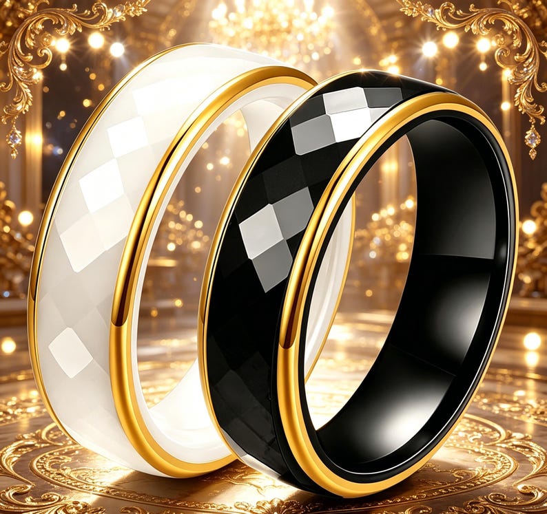 May include: Two rings, one white and one black, with a faceted design. Both rings have a gold-colored band around the edges. The rings are displayed on a gold-colored surface.