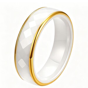 May include: A white ceramic ring with a faceted outer band and a polished inner band. The ring is accented with a gold-colored metal trim on both edges. The ring is a simple, elegant piece of jewelry.