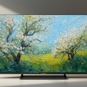 Op de afbeelding: Een zwarte flatscreen-televisie toont een schilderij van bloeiende bomen. Het kunstwerk toont witte bloesems, groen gras en een blauwe lucht. De tv staat op een wit oppervlak.