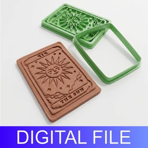 May include: A brown rectangular cookie cutter featuring a raised design of The Sun tarot card with the Roman numeral XIX and the text THE SUN. A separate green rectangular frame cutter is positioned next to it, matching the shape of the card design.