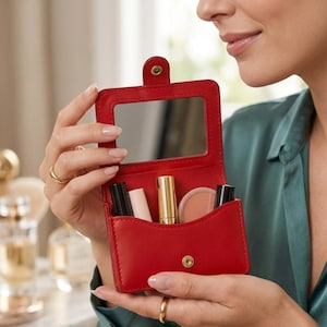 May include: A red leatherette makeup case with a mirror and various cosmetic products. The case is held open, revealing a compact mirror, lipstick, and other beauty items. The case is rectangular with a snap closure.