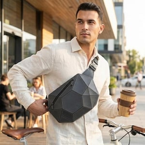 May include: A geometric-patterned black crossbody bag with a zippered pocket. The bag is worn across the body. The person is also holding a reusable coffee cup with a wooden sleeve.