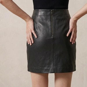 May include: A black leather skirt with a straight silhouette and a visible zipper down the back. The skirt is knee-length and appears to be made of a smooth, high-quality leather. The overall style is classic and versatile.