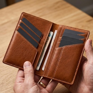 May include: Open brown leather wallet with multiple card slots and cash. The wallet is filled with black cards and folded bills. The wallet is held open, showcasing its interior design and storage capacity.