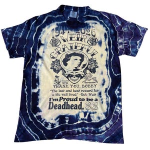 May include: A tie-dye t-shirt with a central graphic featuring a portrait, roses, and the words "Grateful" and "Deadhead." The shirt has a blue and white spiral pattern. Text includes "Thank You, Bobby" and a quote by Bob Weir.