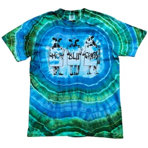 May include: Tie-dye t-shirt with a blue and green spiral pattern. The shirt features three cartoon cows holding signs that read "Moo", "Blu", and "Grass". The design is in black and white.