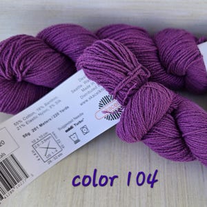 May include: A skein of Posy Petals yarn in color 104, a vibrant purple. The label indicates the yarn is 55% cotton, 16% bamboo, 21% elastic nylon, and 8% silk. The label also shows the yarn weight is 50g and 201 meters/220 yards.