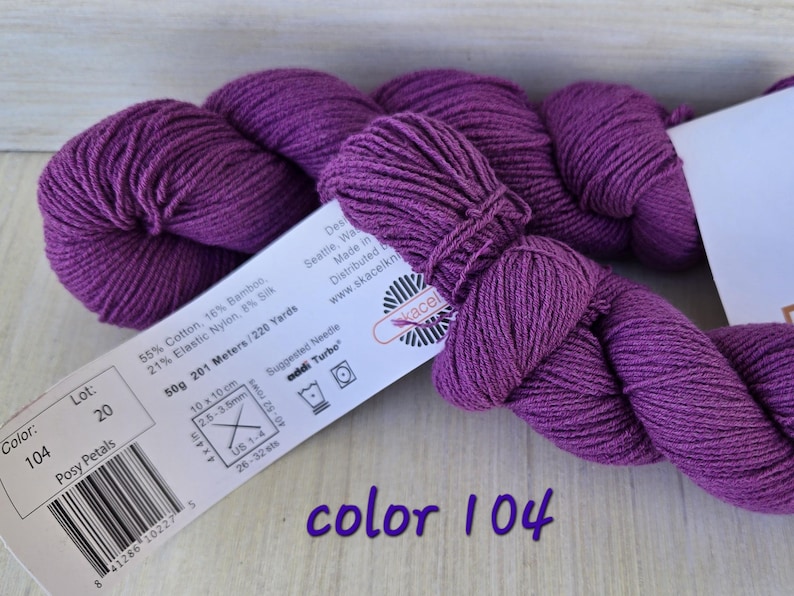 May include: A skein of Posy Petals yarn in color 104, a vibrant purple. The label indicates the yarn is 55% cotton, 16% bamboo, 21% elastic nylon, and 8% silk. The label also shows the yarn weight is 50g and 201 meters/220 yards.