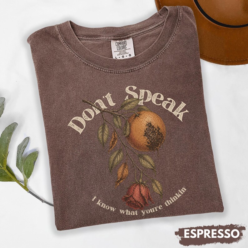 May include: Espresso-colored t-shirt with the text "Don't Speak" and a botanical illustration of a fruit and rose. The shirt is a Comfort Colors brand, and the design includes the phrase "I know what you're thinkin."