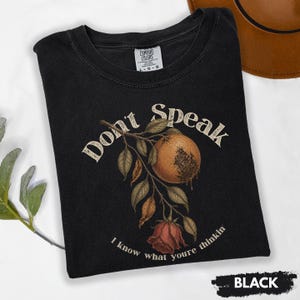 May include: Black t-shirt with a vintage-style botanical design. The graphic features a stylized orange fruit, leaves, and a rose, with the words "Don't Speak" and "I know what youre thinkin".