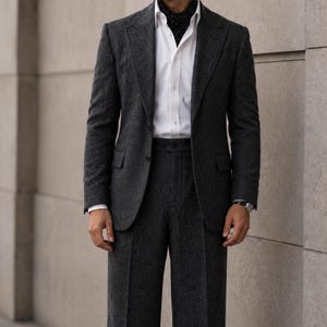 May include: A dark grey suit, comprising a blazer and wide-leg trousers, worn with a white shirt and a black patterned scarf. The image also shows black sunglasses and black dress shoes. The brand name "CLOUTIQ" is visible in the upper left corner.