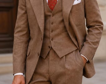 May include: A brown three-piece suit featuring a blazer, a buttoned vest, and trousers. The suit is paired with a crisp white collared shirt, a red patterned necktie, and a white pocket square. A straw hat is held in the lower portion of the frame.