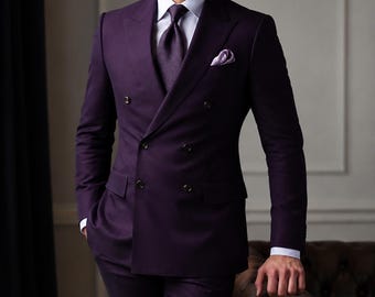 May include: A deep purple double-breasted suit jacket with four dark buttons, paired with matching trousers, a crisp white collared shirt, a textured dark purple tie, and a light purple pocket square. The logo CLOUTIQ is visible in the top corner.